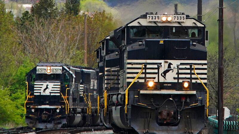 FILE - A Norfolk Southern freight train passes a train on a siding as it approaches a crossing...
